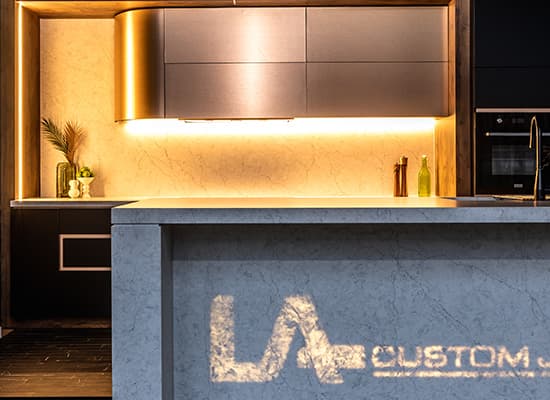 The LA Custom Joinery mark milled straight into a showroom benchtop, beside warm brass and timber cabinetry