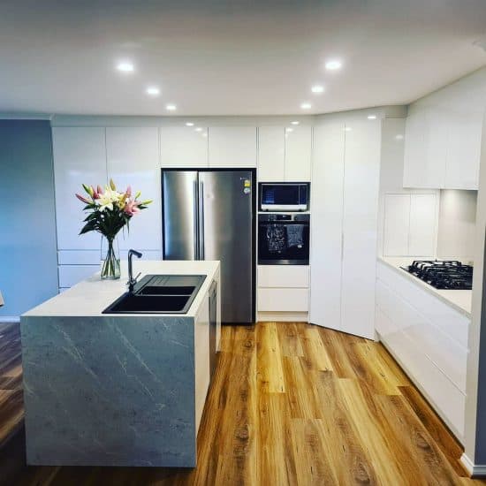 Curved white gloss kitchen with a marble waterfall island and warm timber flooring