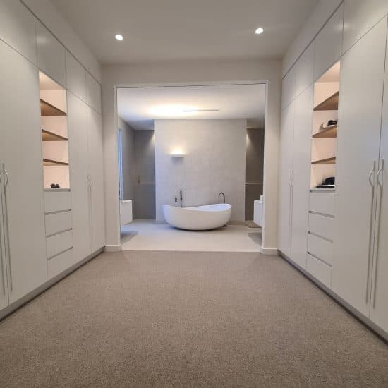 Walk-in robe joinery opening onto an ensuite with a freestanding bath