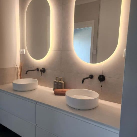 Backlit oval mirrors over a white double vanity