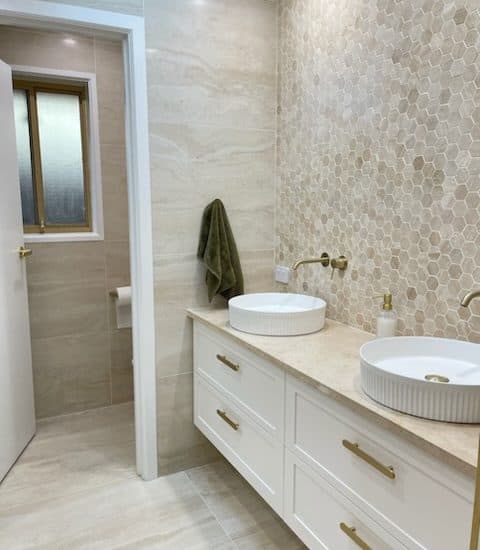 Travertine-tiled ensuite with a hexagon mosaic splashback and brushed-gold tapware