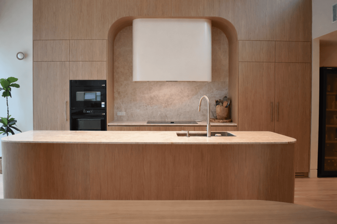 Curved timber kitchen with an arched rangehood nook, waterfall stone island and warm oak cabinetry, a signature LA Custom Joinery build